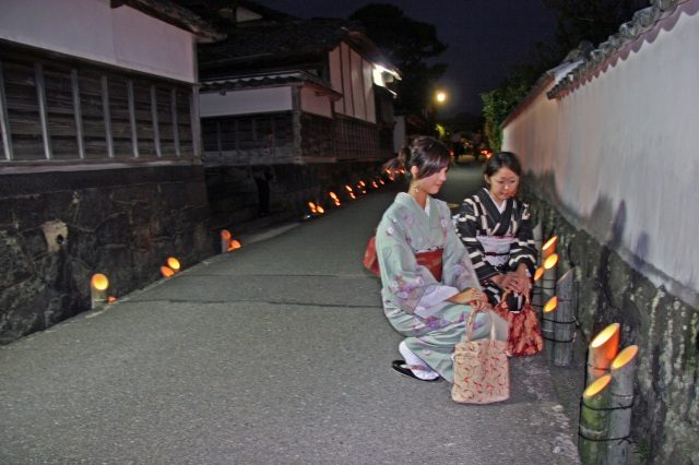 夜の城下町、提灯が並ぶ通りを着物姿で歩く様子